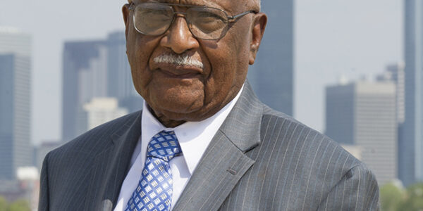 Dr. Claude Williams stands in front of the Dallas skyline.