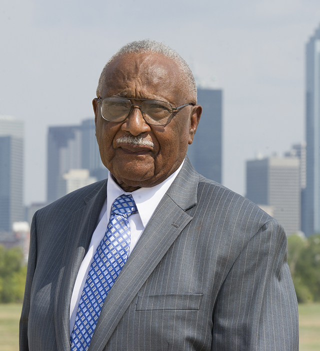 Dr. Claude Williams stands in front of the Dallas skyline.