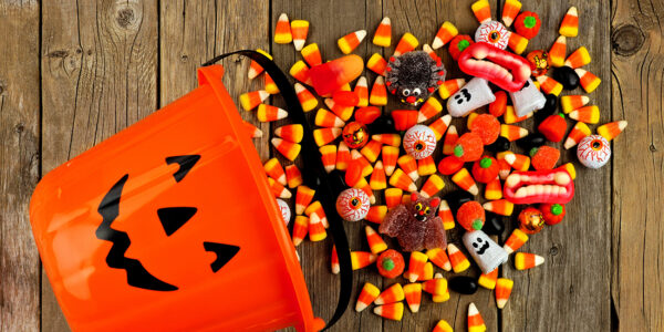 Halloween Jack o Lantern pail with spilling candy, above view on a rustic wood background