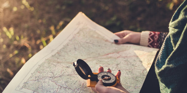 Traveler young woman searching direction with a compass on background of map in the forest