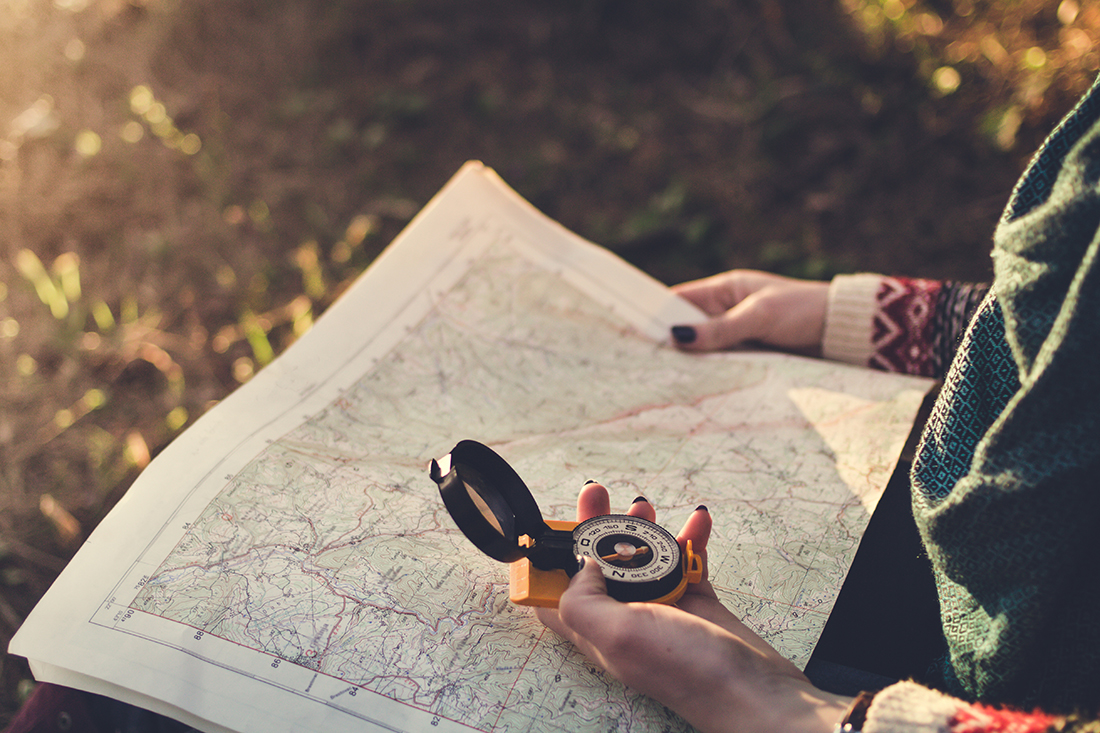 Traveler young woman searching direction with a compass on background of map in the forest