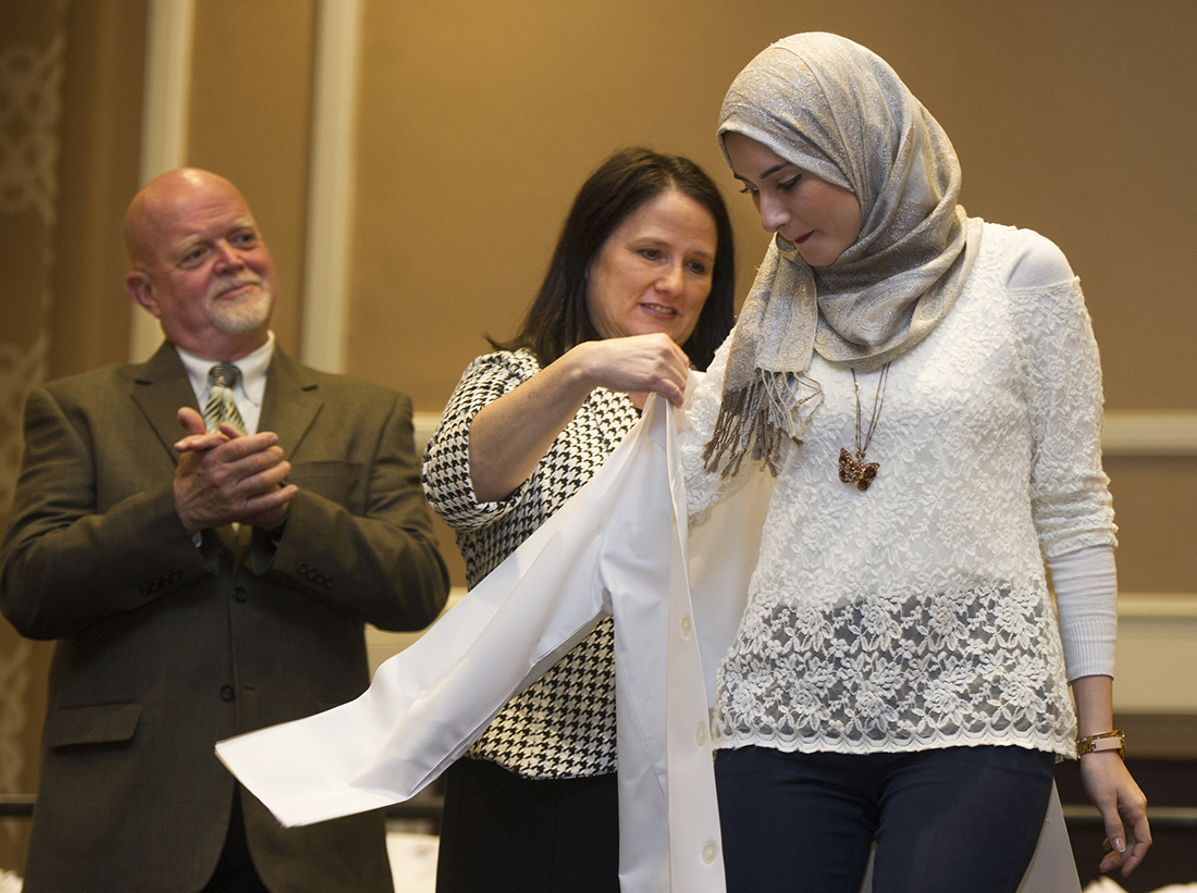 Texas A&M College of Dentistry Alumni Association President Laurie Inglis helps a student into her white coat.