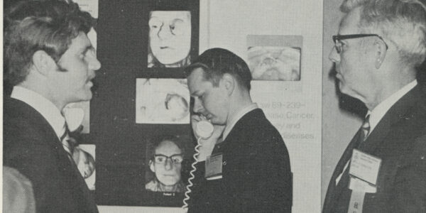 Dr. Roy Rinkle (left) and Dr. Kenneth Randolph (right) at the maxillofacial prosthetic center's exhibit during the Dallas Mid-Winter Clinic in 1971. Dr. Mack Charles Hughes (center), then a senior dental student, listens to one of the exhibit's tape recordings.