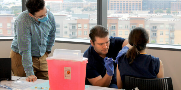 Fourth-year dental student Travis Horn practices his injection technique on a classmate under the watchful eye of a College of Pharmacy student.